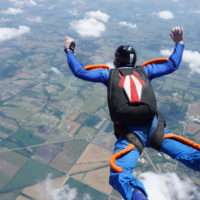 man in freefall wearing black Sun Path skydiving rig with red and white details