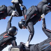formation skydiving team in freefall wearing matching black, blue and red Sun Path rigs